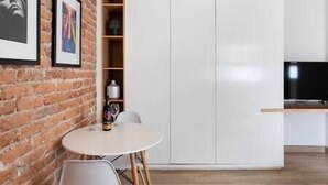A modern kitchen with white cabinets, a brick wall, a round table with chairs, and a television. - Cozy · Cozy apartment great location (Mexico City)