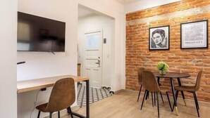 A modern dining area with a brick wall, a flat-screen TV mounted above a white door, and a small table with chairs. - Alvaro · Great location. Renovated apartament in Roma Norte (Mexico City)
