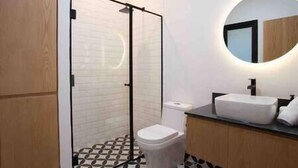 A modern bathroom with a glass shower enclosure, a white toilet, and a round mirror above a sink with a black countertop. - Alvaro · Great location. Renovated apartament in Roma Norte (Mexico City)