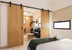 A modern bedroom with a bed, a sliding door, a small seating area, and a brick wall.
