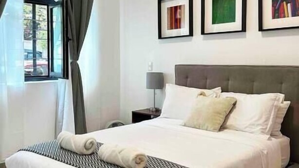 Quarto de hotel com uma cama, uma mesinha de cabeceira, um abajur e três quadros na parede.