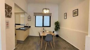Uma área de refeições compacta com mesa e cadeiras de madeira, pequena cozinha com pia, e uma janela que proporciona iluminação natural.