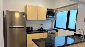 Uma cozinha moderna com eletrodomésticos de aço inoxidável, armários de madeira clara e bancada preta.
