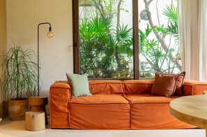 Ein modernes Wohnzimmer mit einem Ecksofa, einem Holztisch und einem großen Fenster mit Blick auf üppiges Grün.