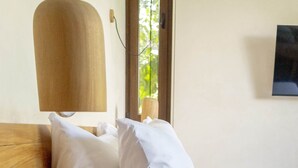 A neatly made bed with white bedding, a wooden headboard, and a round wooden stool in a room with a simple, clean design. - Room with Private Terrace and Pool |• TEVA 3B (Tulum)