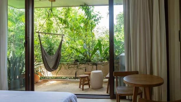A room with a large sliding glass door leading to a balcony with a hammock, wooden chairs, and a round table. - Room with Private Terrace and Pool |• TEVA 3B (Tulum)