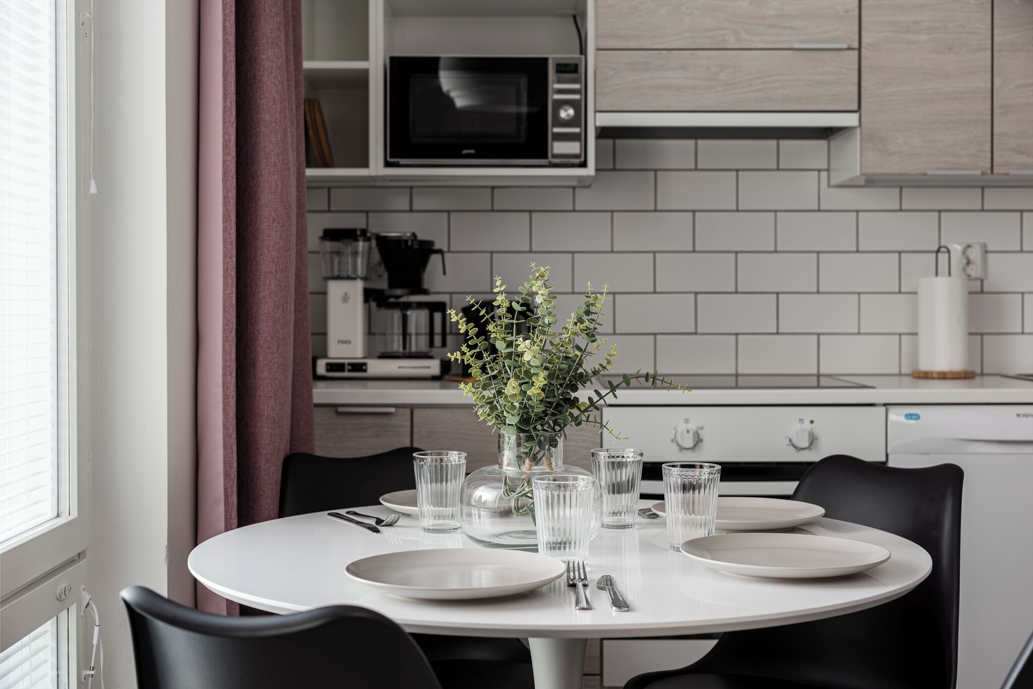 A modern kitchen with white cabinets, a microwave, and a dining table set for four.