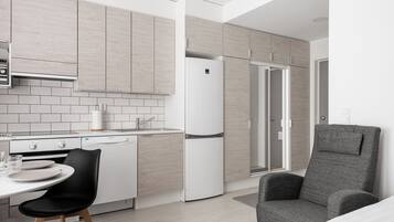Eine moderne Küche mit hellen Holzschränken, einem weißen Kühlschrank und einem Essbereich mit einem schwarzen Stuhl.