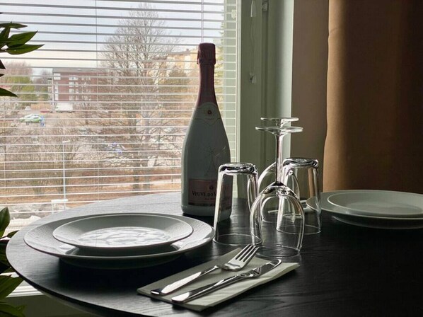 A table set with plates, cutlery, and a bottle of Veuve Clicquot wine, with a window view in the background. - Borg Housing Travel Center (Pori)