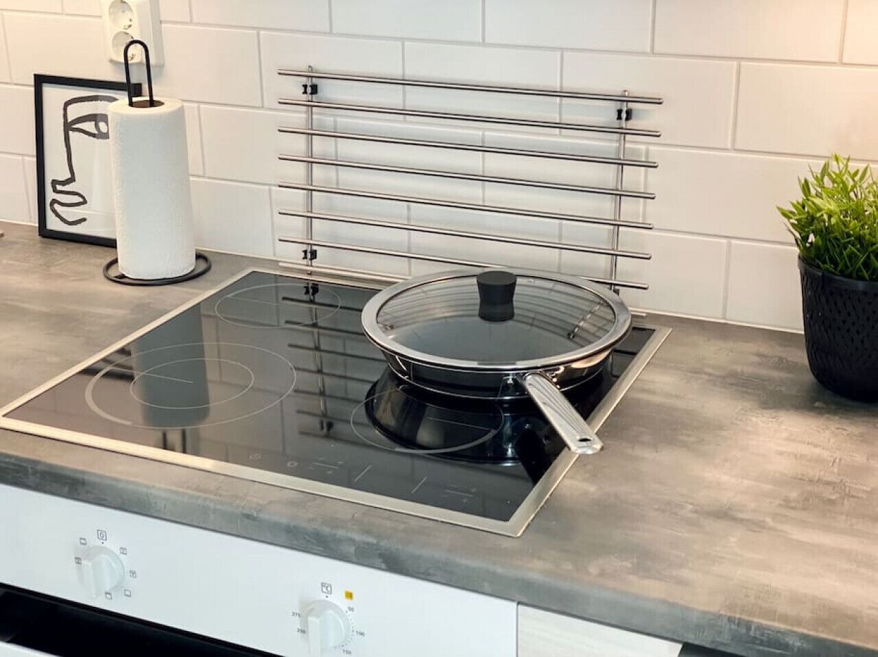 A kitchen with a glass-top stove, a pot rack, a roll of paper towels, and a potted plant.