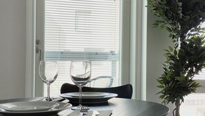 A dining table with plates, cutlery, and wine glasses, set against a window with blinds. - Borg Housing Travel Center (Pori)