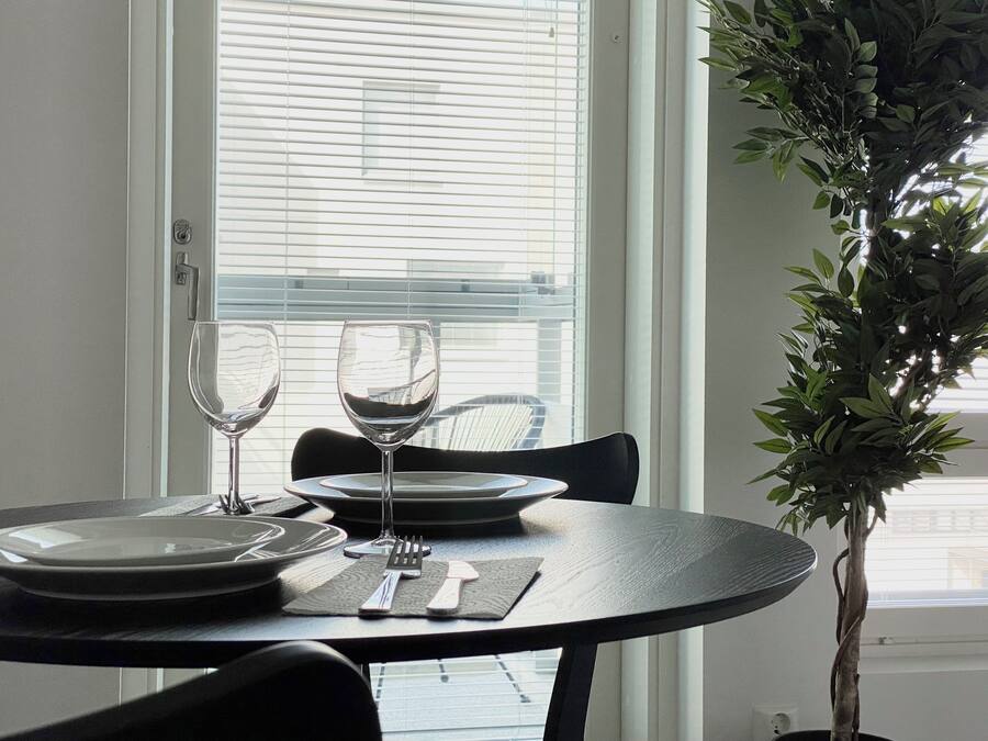 A dining table with plates, cutlery, and wine glasses, set against a window with blinds.