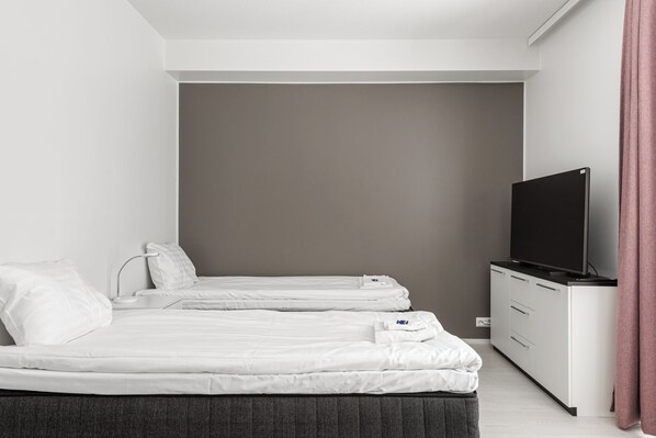 Una habitación de hotel con dos camas individuales, un televisor sobre una cómoda y una pared gris.