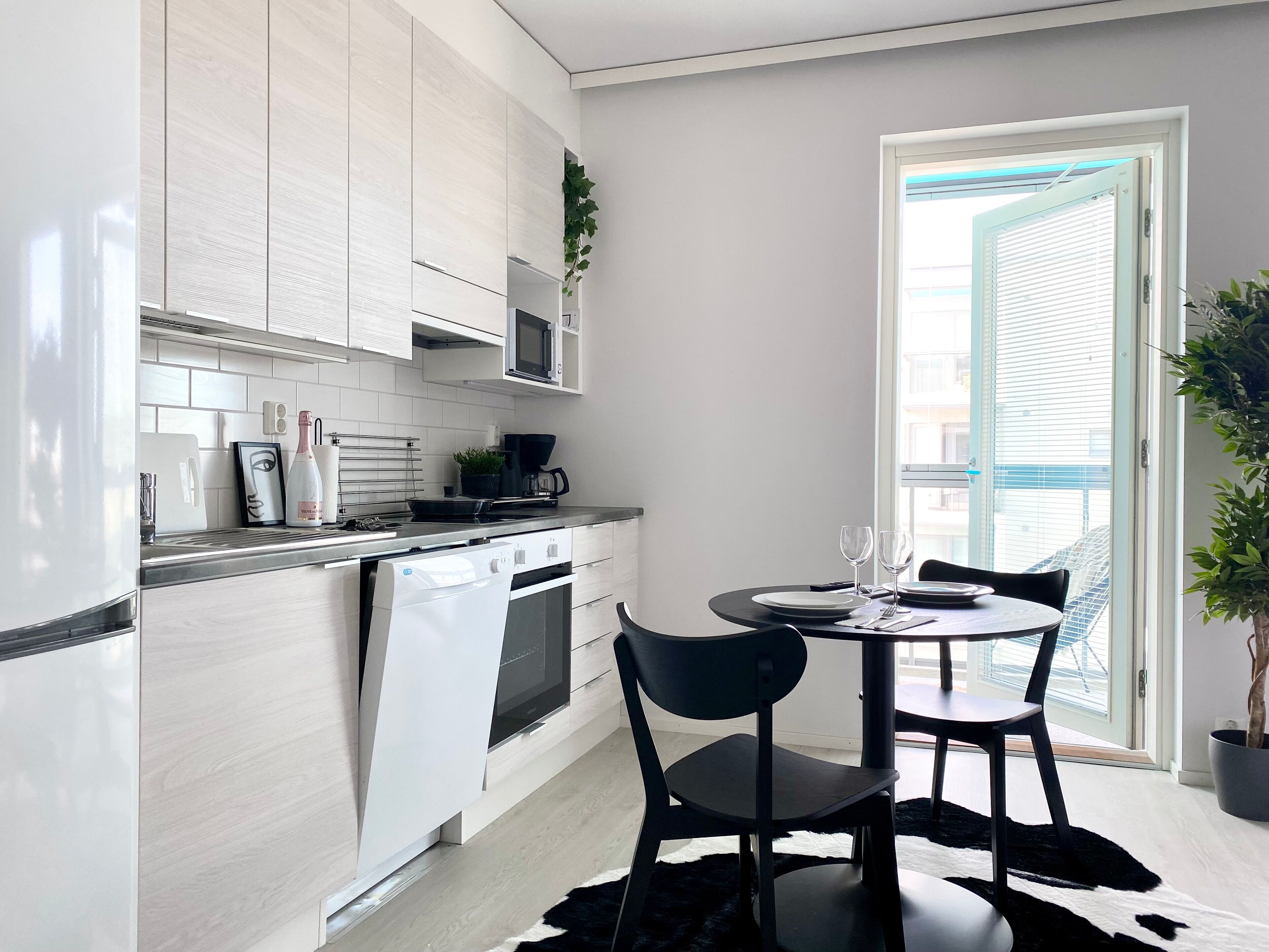 A modern kitchen with white cabinetry, a built-in oven, and a microwave. There is a dining area with a round table and two chairs.
