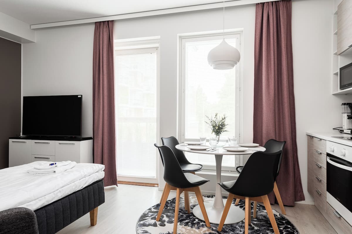 Ein modernes Hotelzimmer mit Bett, Fernseher, Essbereich mit Tisch und Stühlen sowie Küchenzeile.