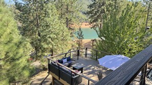 Une terrasse avec des sièges extérieurs et une vue sur un lac entouré d’arbres.