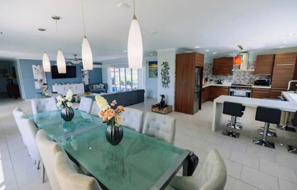 Una cocina moderna con una isla central, iluminación colgante y una zona de comedor con mesa y sillas de vidrio.