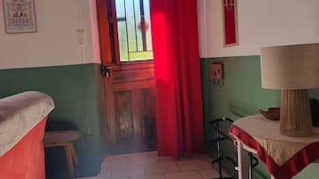Una habitación con techo de madera, una cortina roja, un taburete pequeño, una mesa con una lámpara y una pared verde.
