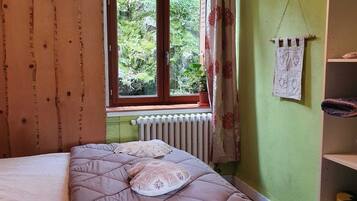 A room with a bed, a window with curtains, a radiator, and a shelf with items.