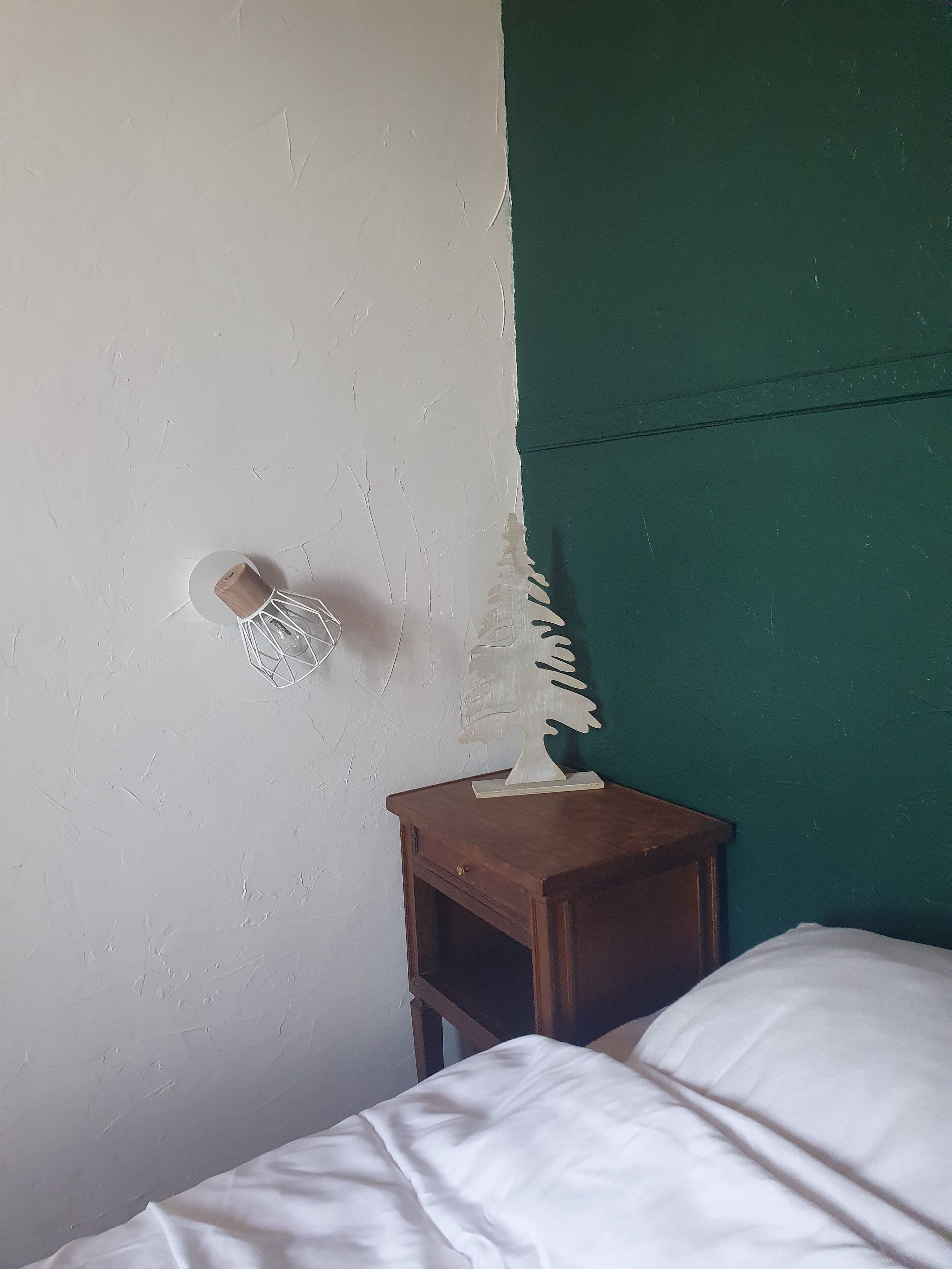 Et værelse med en hvid væg, en grøn accentvæg, et trænatbord med en hvid genstand på, samt en seng med hvidt sengetøj.
