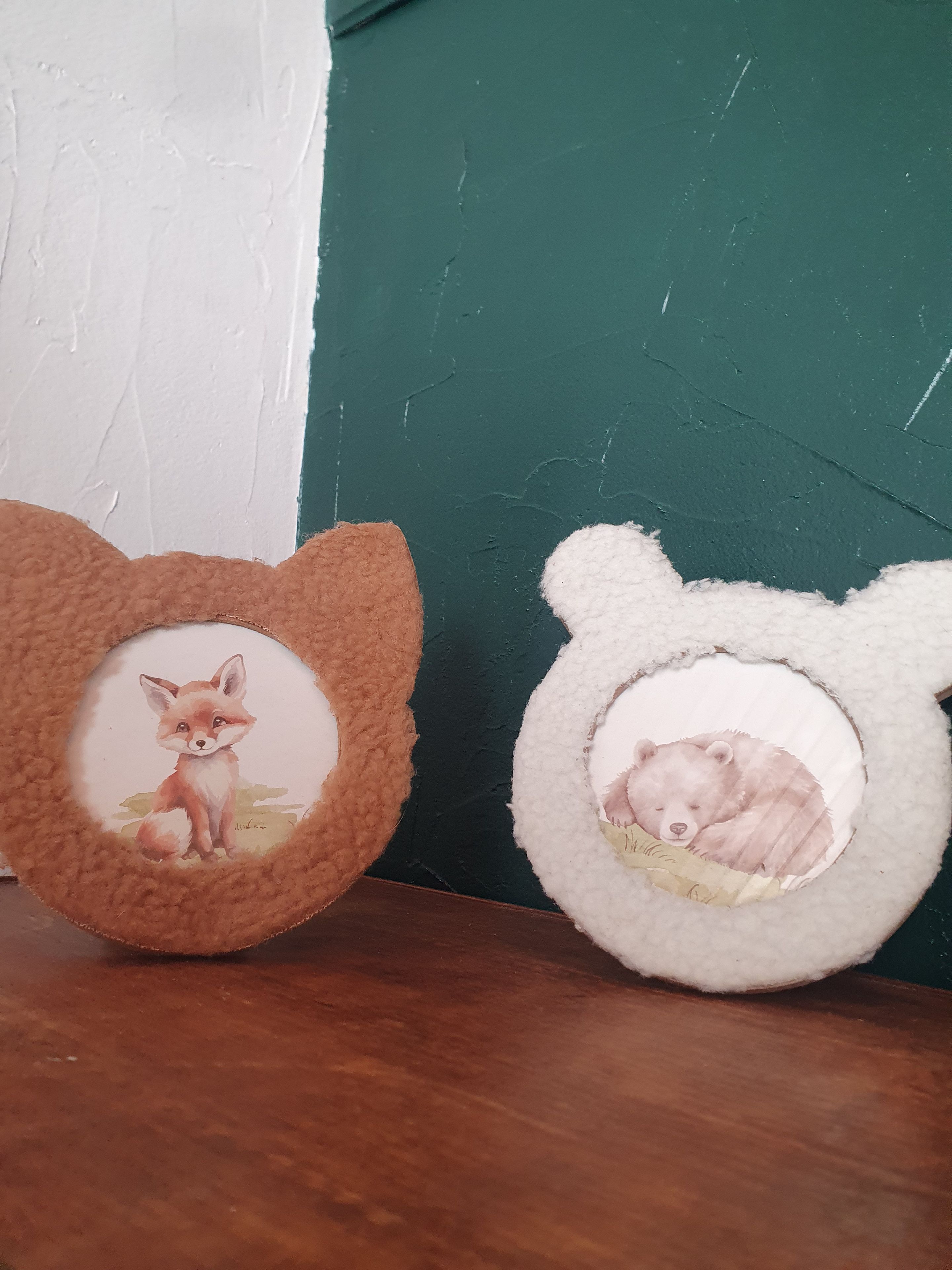 Zwei weiche, tierförmige Kissen mit Tierbildern auf einer Holzfläche.