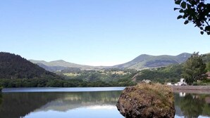 Un lac paisible où une petite barque est amarrée au bord, entouré d’une végétation luxuriante et dominé par des collines lointaines.