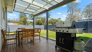 An outdoor patio with a grill, wooden furniture, and a covered area. - Huskisson Delight! by Experience Jervis Bay (Huskisson)