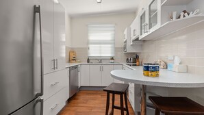 A compact kitchen with white cabinets, a built-in oven, and a window with blinds. - Huskisson Delight! by Experience Jervis Bay (Huskisson)