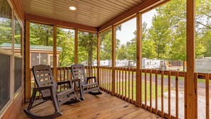 A covered porch with wooden flooring and a railing, overlooking a campground with RVs and trees. - Sun Outdoors Lake Rudolph (Santa Claus)