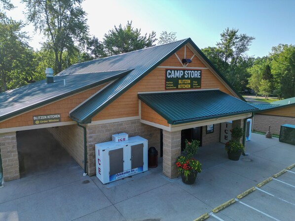 A camp store with a signboard listing items like nachos, pretzels, sandwiches, and ice cream.