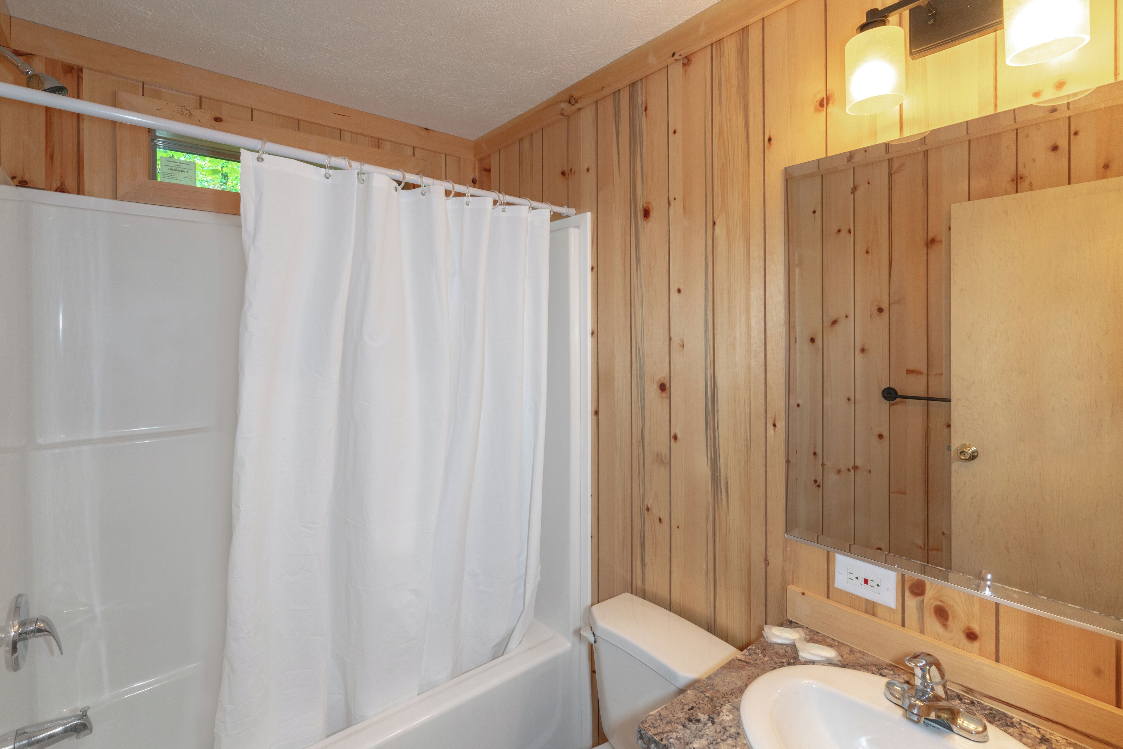 A wooden-paneled bathroom with a bathtub, a shower curtain, a sink, and a mirror.