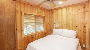 A bedroom with wooden walls, a bed with white bedding, a window with blinds, and a ceiling fan. - Sun Outdoors Lake Rudolph (Santa Claus)