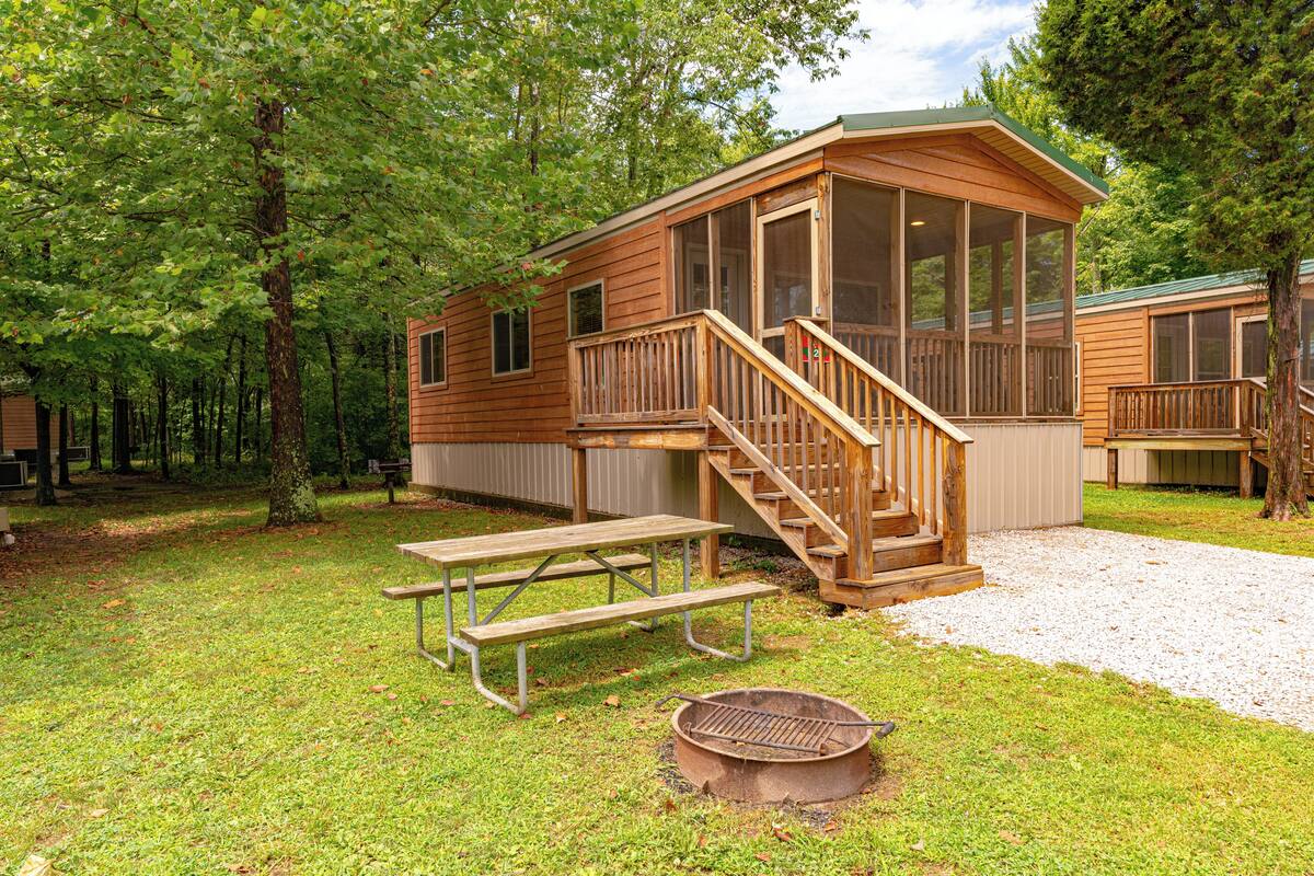 A wooden cabin with a porch, a picnic table, and a fire pit.