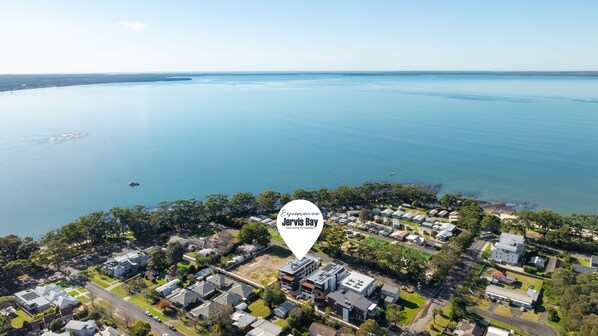 An aerial view of a coastal residential area with houses, roads, and a large body of water. - HuskySun by Experience Jervis Bay (Huskisson)