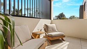A balcony with two cushioned chairs, a small wooden table, and a glass of wine. - HuskySun by Experience Jervis Bay (Huskisson)