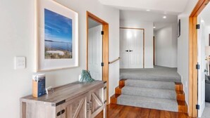 A hallway with a wooden console table, a framed picture on the wall, and a staircase with grey carpet leading to a room.