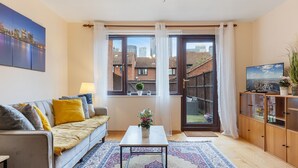 Una sala de estar moderna con un sofá, una mesa de centro y vistas de un paisaje urbano a través de amplios ventanales.