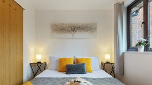 Un dormitorio con cama, dos mesitas de noche, una ventana con vistas y una obra de arte colgada en la pared.