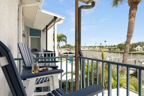 A balcony with a table and chairs, overlooking a marina with boats and palm trees.