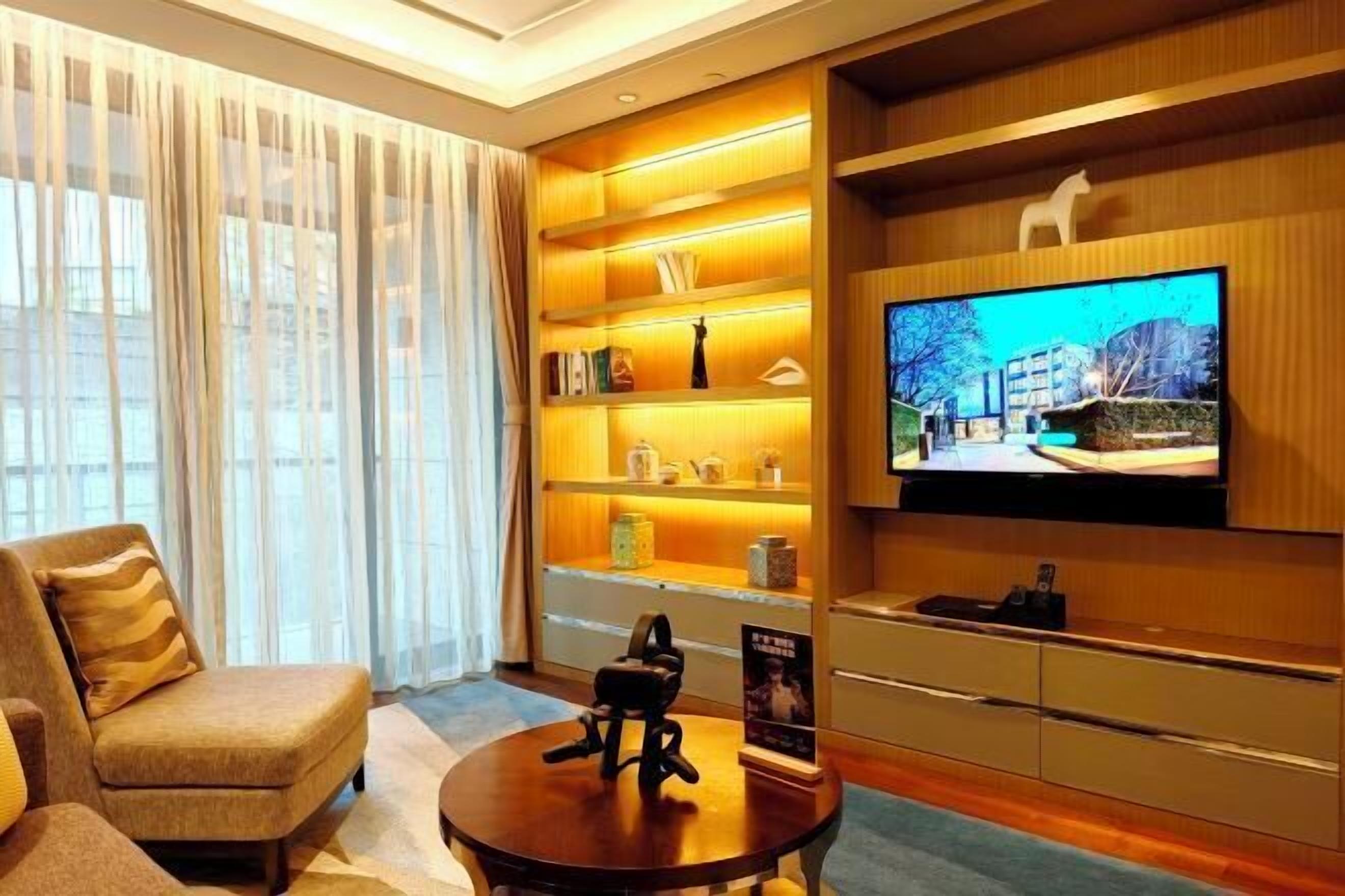 A modern living room with a sofa, a coffee table with a VR headset, a TV mounted on the wall, and a bookshelf with various items.