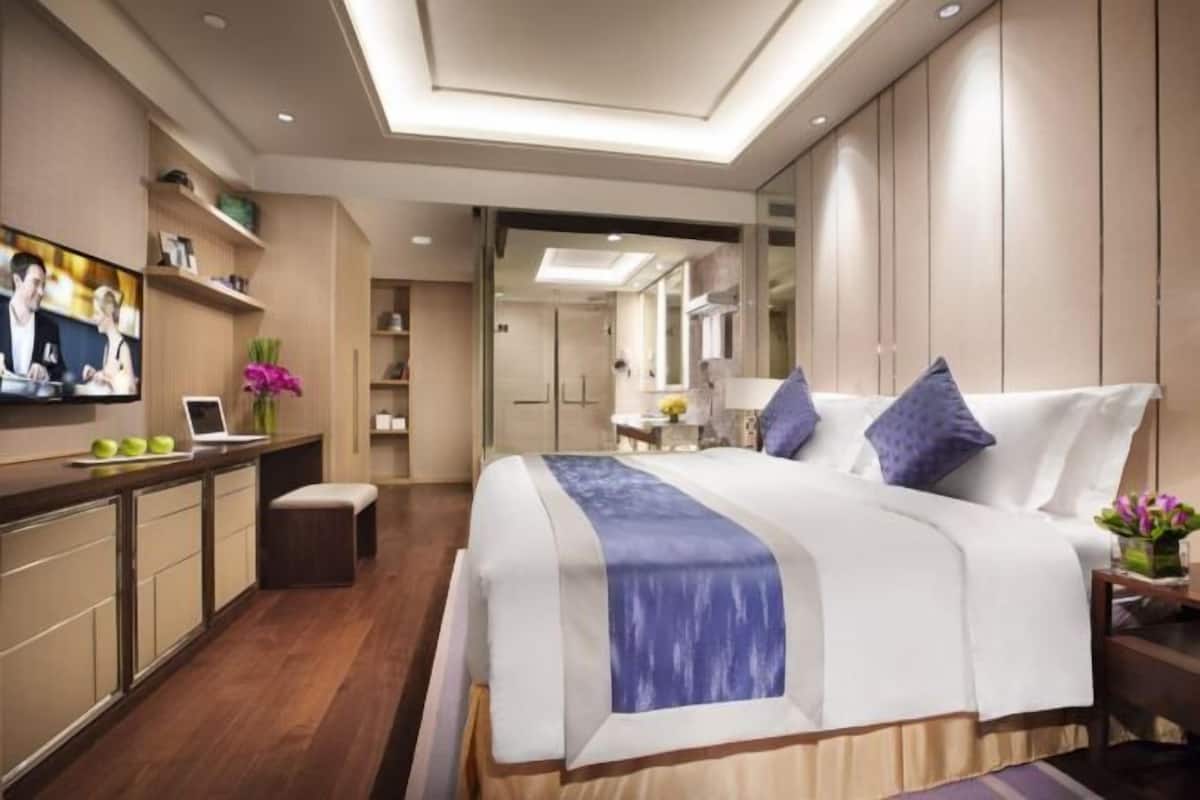 A modern hotel room with a large bed, a desk with a laptop, a TV, and a bathroom visible through an open door.