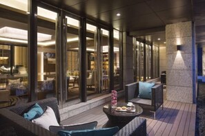A modern outdoor seating area with wicker furniture and a coffee table, overlooking a well-lit interior space with glass doors. - Ascott Heng Shan Shanghai (Shanghai)