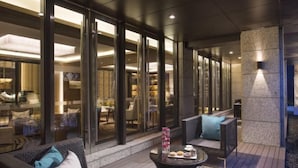 An outdoor seating area with wicker furniture and a coffee table, overlooking a restaurant with glass doors. - Ascott Heng Shan Shanghai (Shanghai)