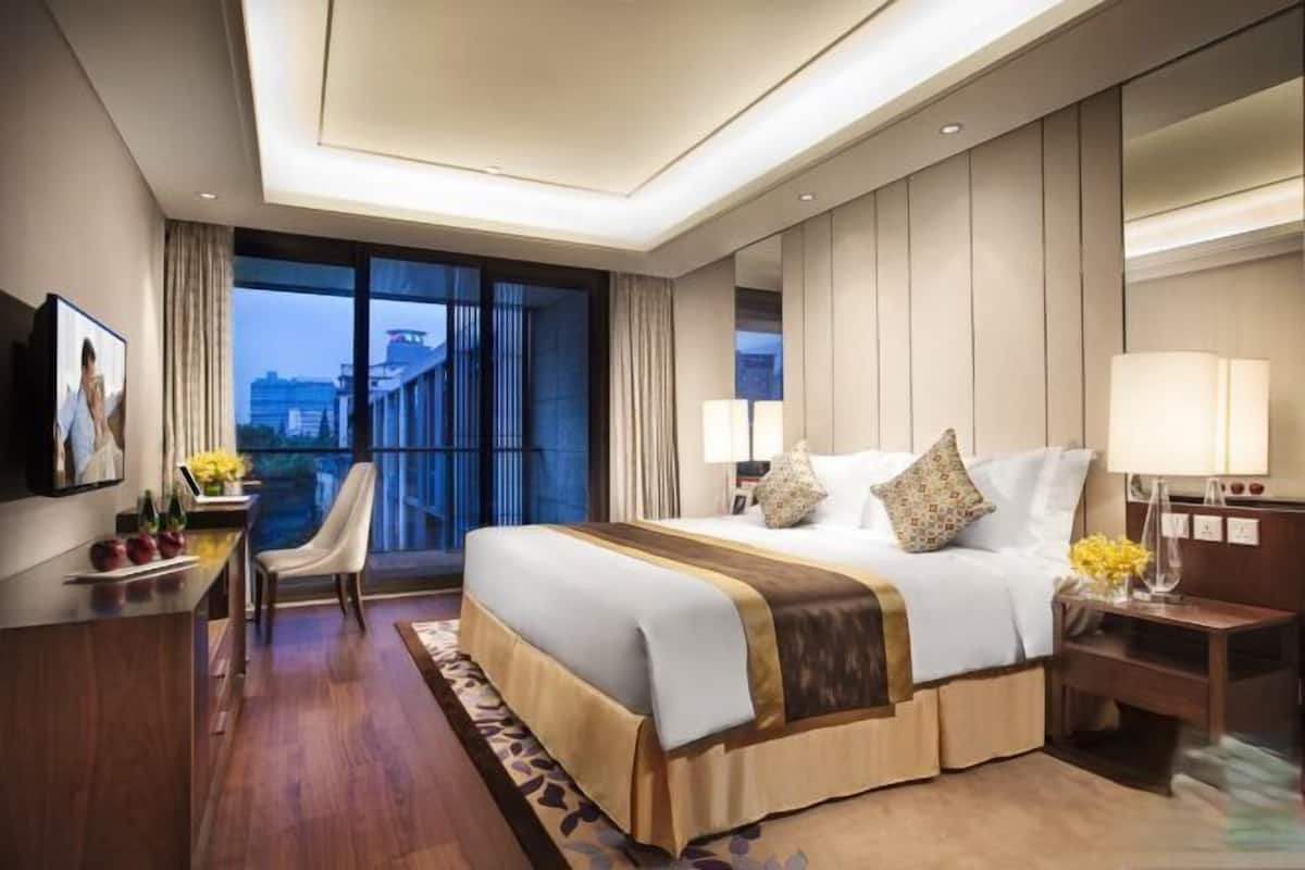 A hotel room with a large bed, a desk, a chair, and a view of the cityscape.