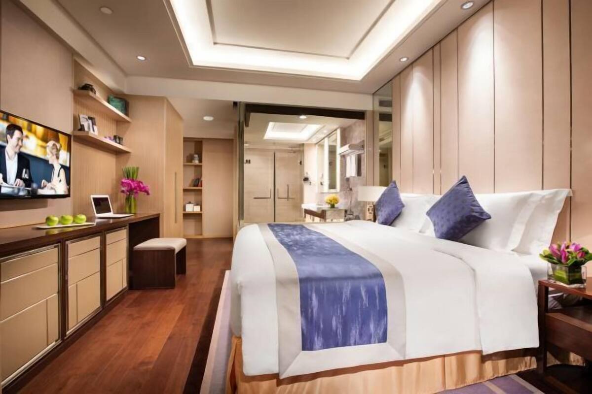A modern hotel room with a large bed, a desk with a laptop, and a television on the wall.