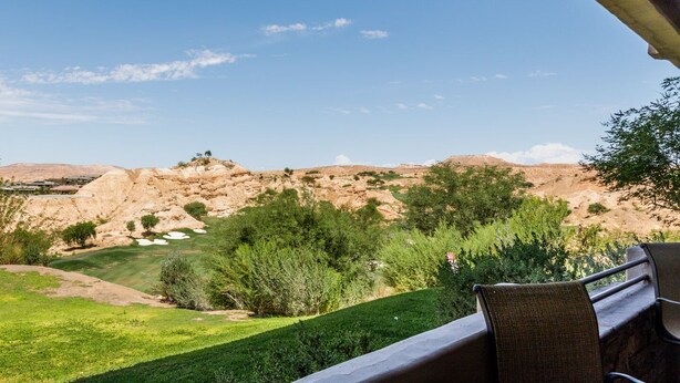 Eine Terrasse mit Tisch und Stühlen mit Blick auf eine angelegte Grünfläche und eine Wüstenlandschaft.