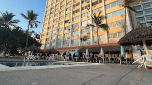 A high-rise hotel with multiple balconies, a pool area with lounge chairs, and palm trees. - Islas del Sol (Mazatlán)