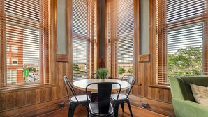 Un coin repas avec une table ronde, des chaises noires et des stores en bois.
