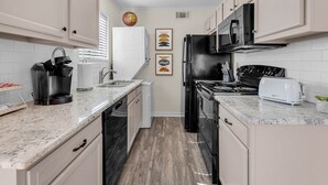 Une cuisine de taille réduite avec des meubles blancs, un réfrigérateur noir, une cuisinière et un grille-pain.
