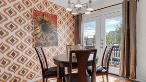 Un coin repas agrémenté d’un mur à motifs, d’un grand tableau représentant un tournesol et d’une vue sur l’extérieur, visible à travers une porte vitrée.